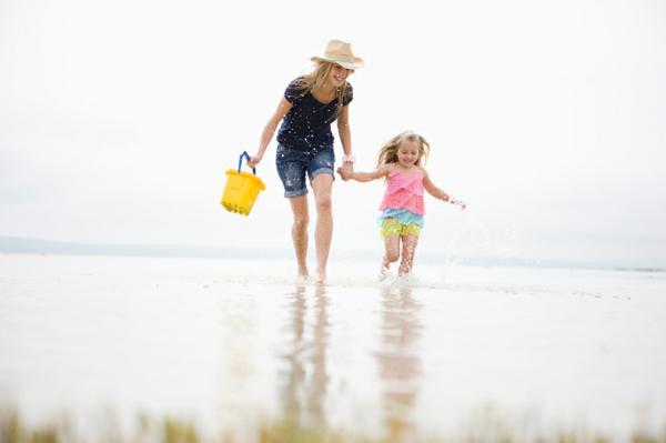 image of mother and young daughter holding hands and walking in the water at the beach