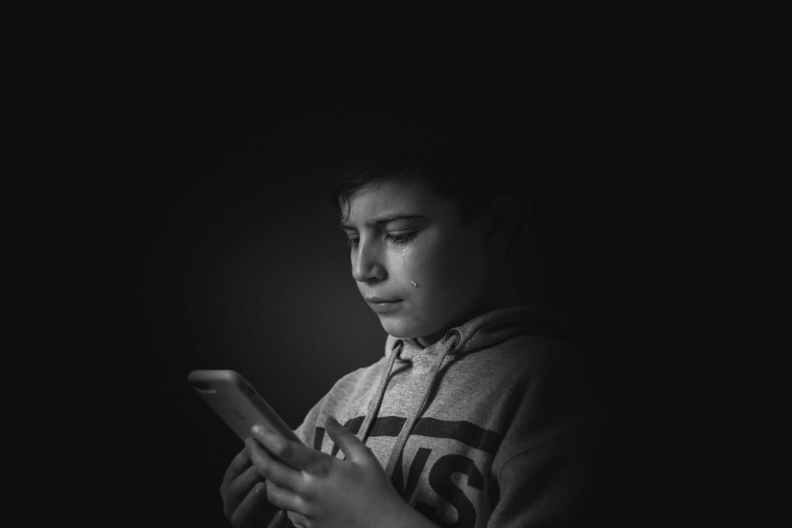 Boy holding smartphone with a tear on his cheek
