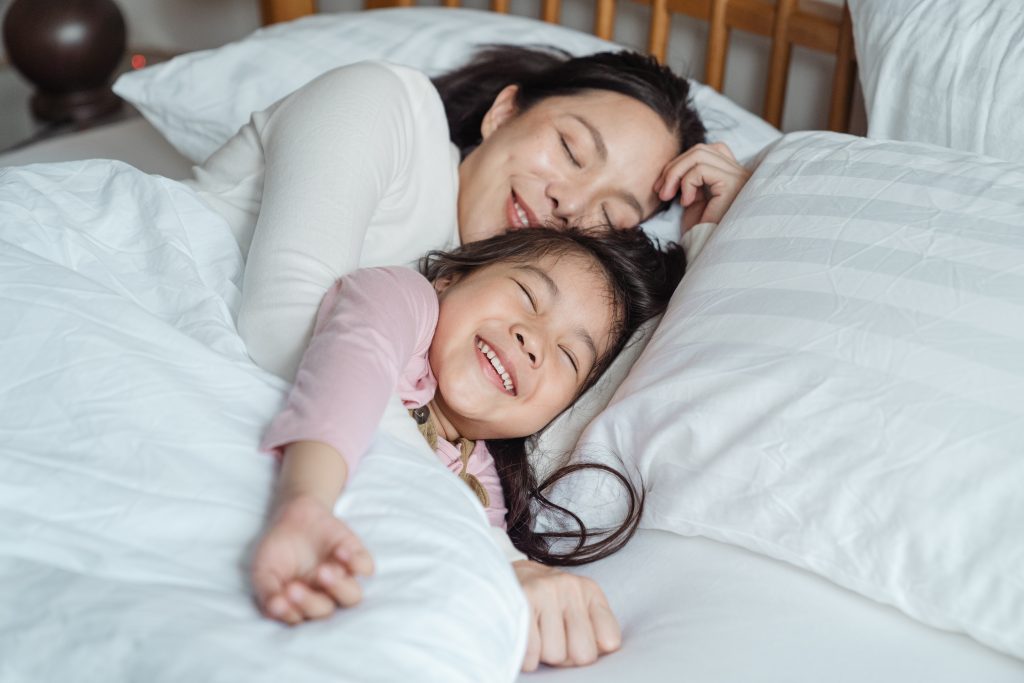 Mother and young daughter happily snuggling in bed together